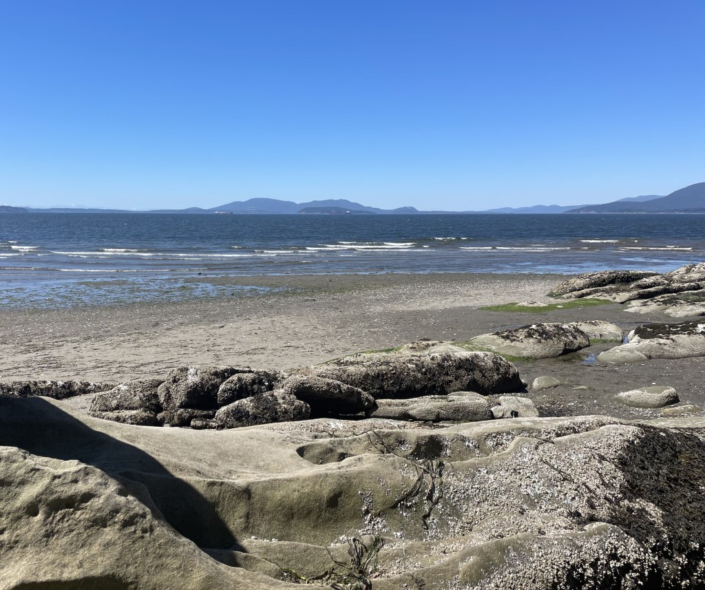 Beach with rocks and sands. Water behind and mountains in the distance.