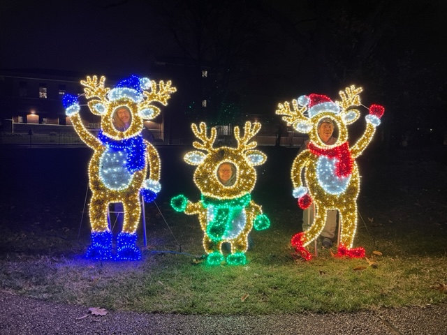 Three cartoonish light-up reindeer, standing upright & waving, with people faces visible in cutouts.