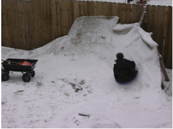 Child riding saucer sled, seen from back.