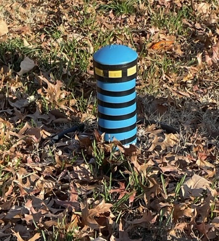 Water pipe sticking up from ground, painted like a lighthouse with blue and black stripes.