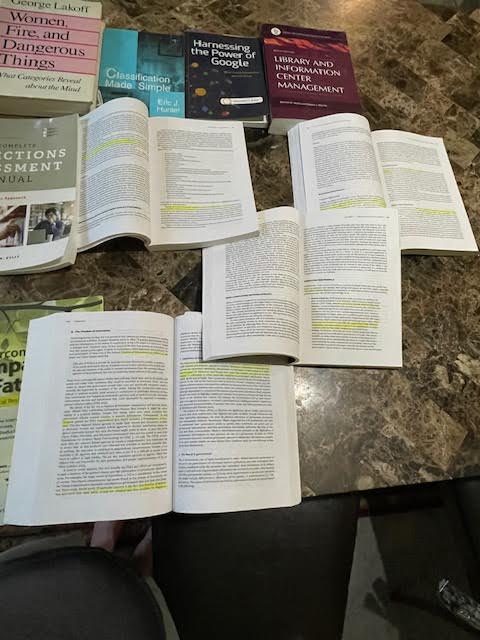 Several books lying flat on a table, some of them opened with highlighted text visible but not readable.