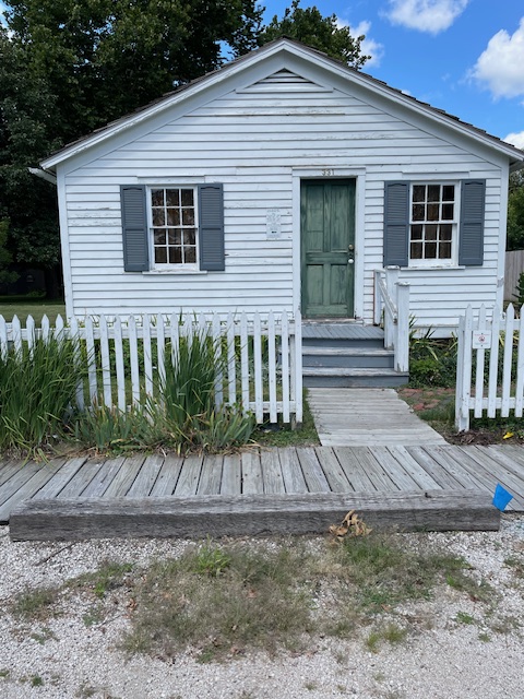 Small white clapboard house with wooden walkway in front and white picket fence.