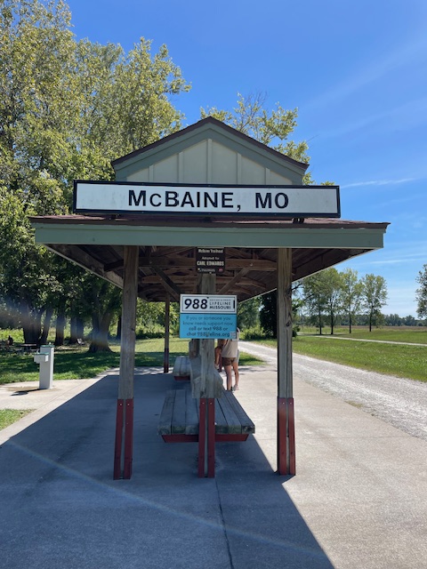 Wooden shelter over benches with sign reading "McBaine, MO"
