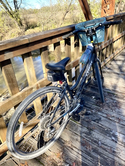 Black bicycle with blue basket leaning on wooden bridge rail.