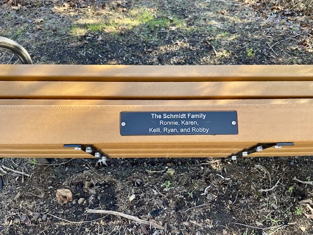 Bench seen from top with little plaque reading "The Schmidt Family: Ronnie, Karen, Kelli, Ryan, and Robby."