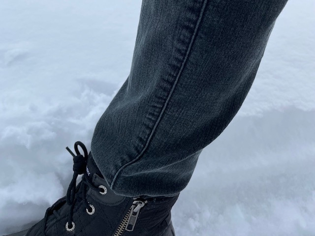 Close up of booted foot (black snow boot) with jeans tucked in and snow more than ankle high behind