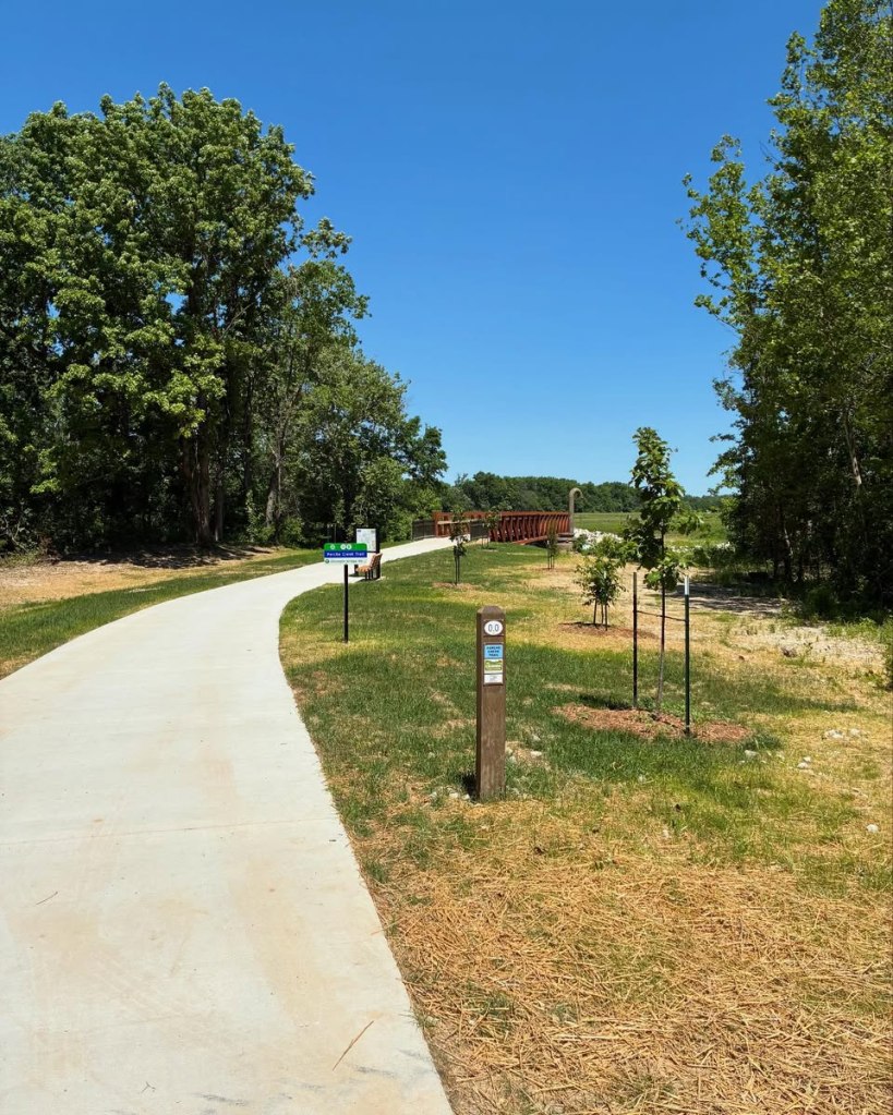 Paved bike trail approaching a bridge. Sign says Perche Creek Trail.