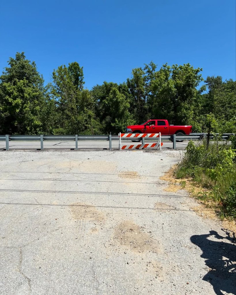 paved trail ending at guardrail with road on other side. Red pickup on road.
