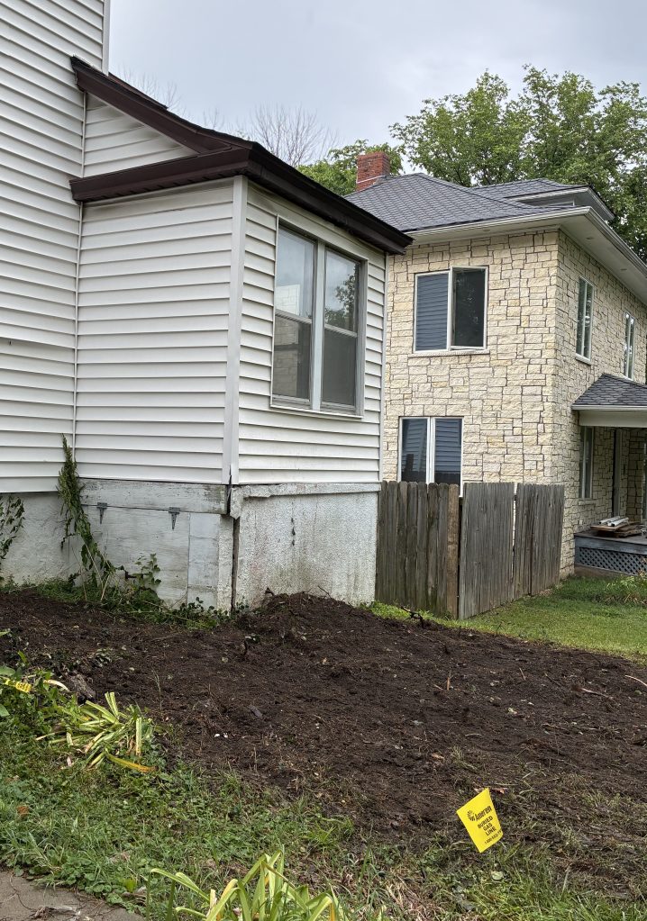 Bare earth in front of a house with white siding.