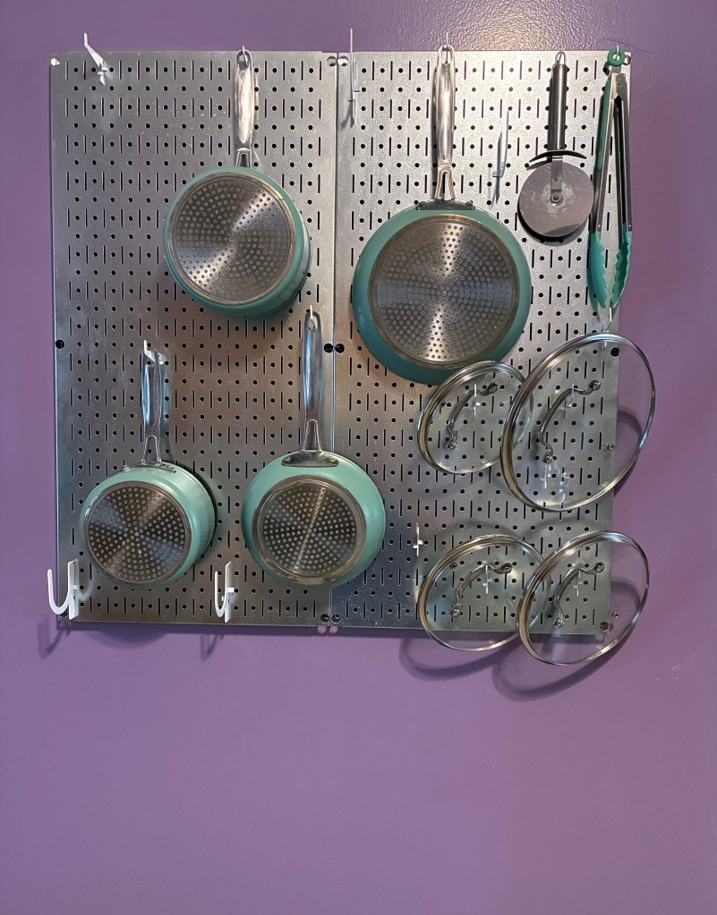 Cookware hanging on a stainless steel rack attached to a purple wall