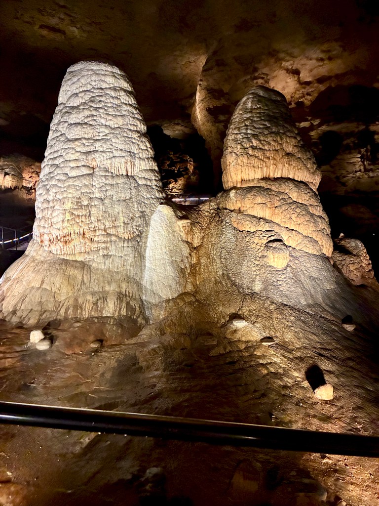 Two large pillars--onne white, one rust colored--rising from a cave floor.