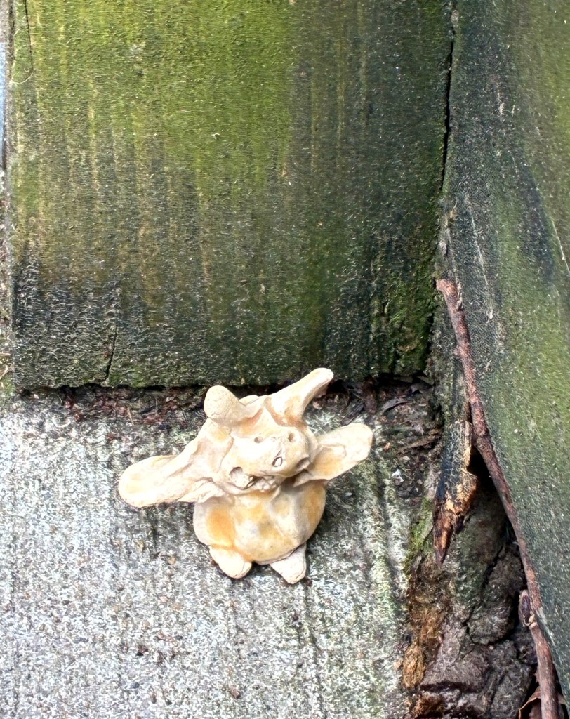 Small clay figure, yellow and beige-sh, of an unidentified creature, in the corner of two moss-covered walls.